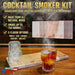 Cocktail smoker kit with a glass of cocktail on a wooden surface, featuring smoke and product packaging.
