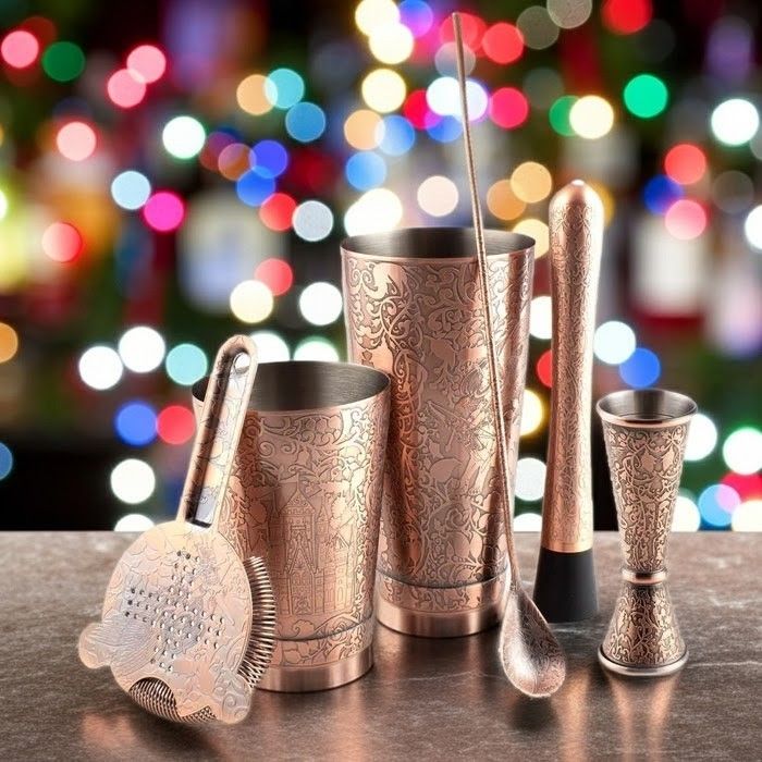 Set of copper cocktail shakers and tools with a festive, blurred multicolored light background.
