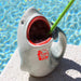 Shark-shaped mug with open mouth and straw, featuring a Tiki Bar logo, against a pool background.