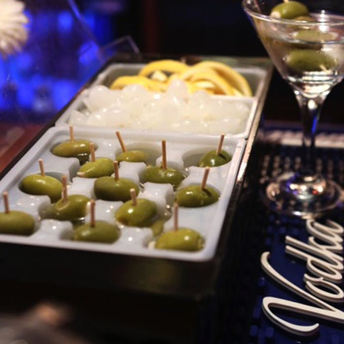 Tray of olives on ice with a cocktail glass in the background