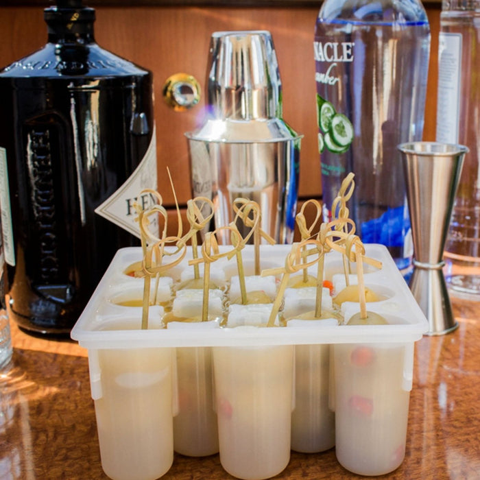 Beverage in ice cube trays with bottles and a cocktail shaker in the background