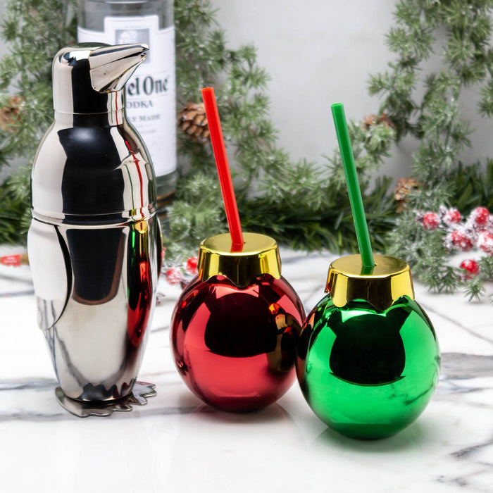 Metallic penguin shaker with red and green Christmas-themed shot glasses on a marble surface.