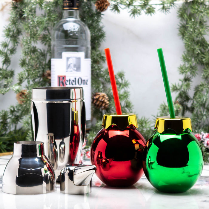 Two metallic Christmas ornament glasses with red and green straws, a bottle of Ketel One vodka in the background.