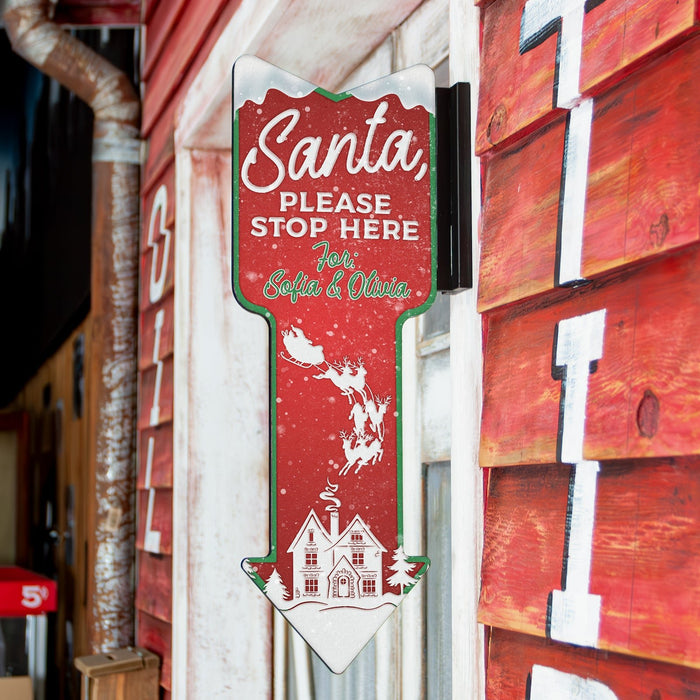 Decorative sign with 'Santa, Please Stop Here' text on a red background with white text and graphics.