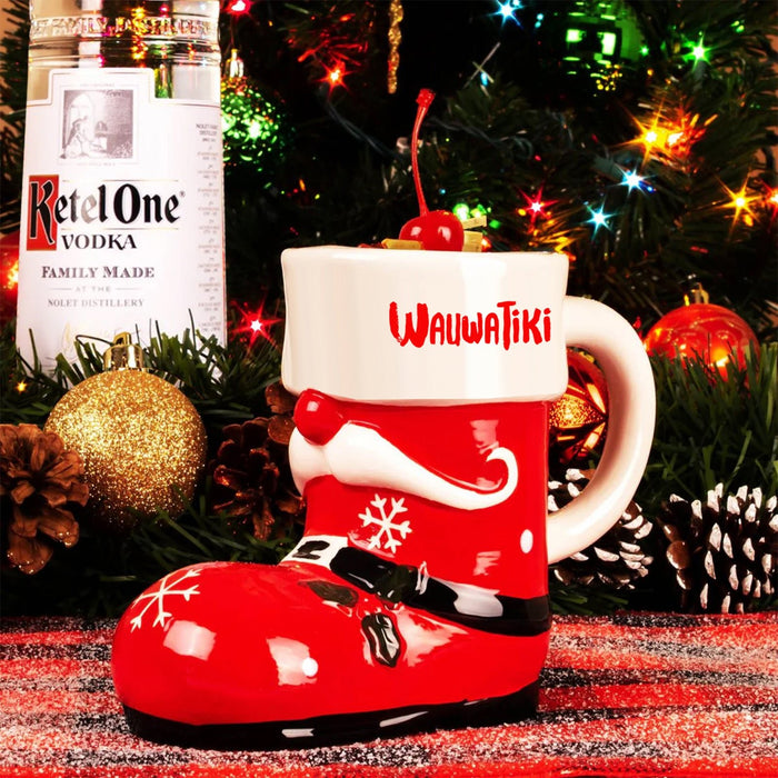 Red Santa boot mug with 'Wauwatiки' branding next to a bottle of Ketel One Vodka against a festive background.