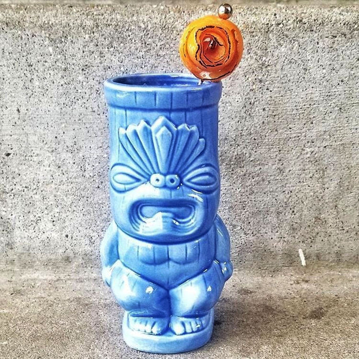 Blue ceramic tiki mug with a decorative top on a concrete surface