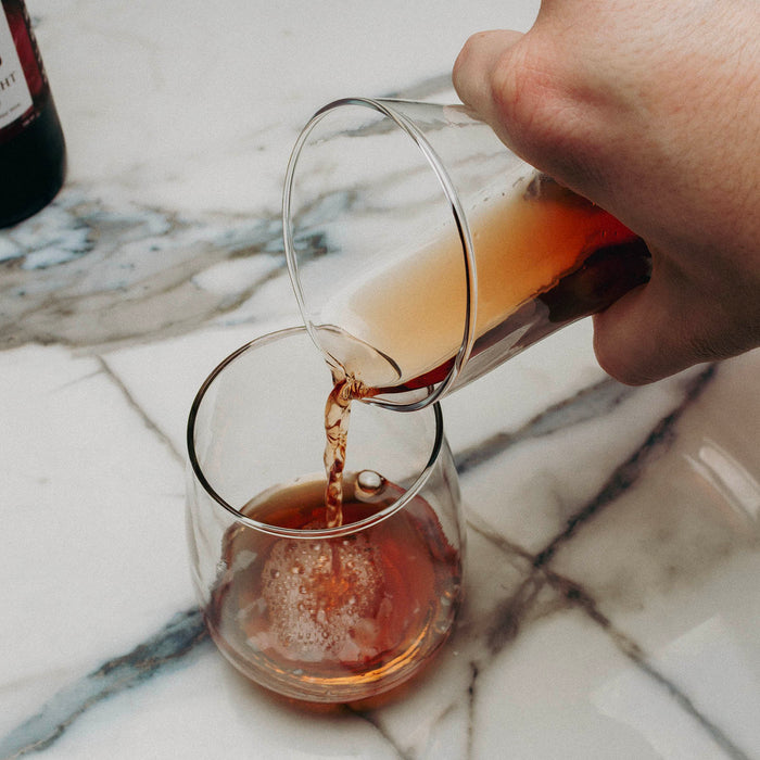 Hand pouring a dark liquid from one glass into another on a marble surface