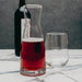 Glass carafe with red liquid and a wine glass on a marble surface