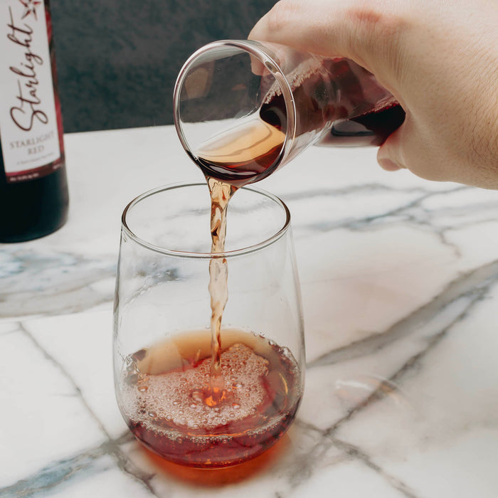 Hand pouring red wine from a bottle into a glass on a marble surface.