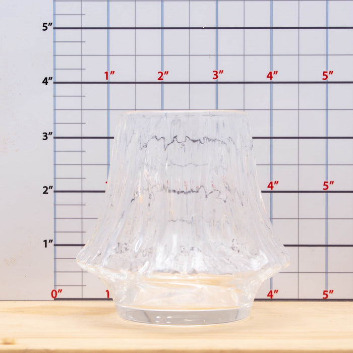 Clear glass candle holder on a wooden surface with a ruler for scale.