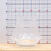 Clear glass candle holder on a wooden surface with a ruler for scale.