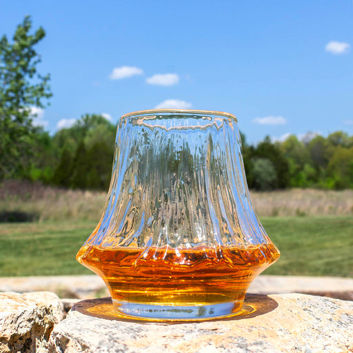 Glass of amber liquid on a rock with a natural background