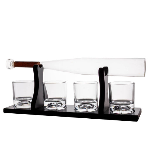 A whiskey decanter set with a clear glass bottle resting horizontally on a black metal stand, with four matching clear glass tumblers on the base, photographed on a white background.