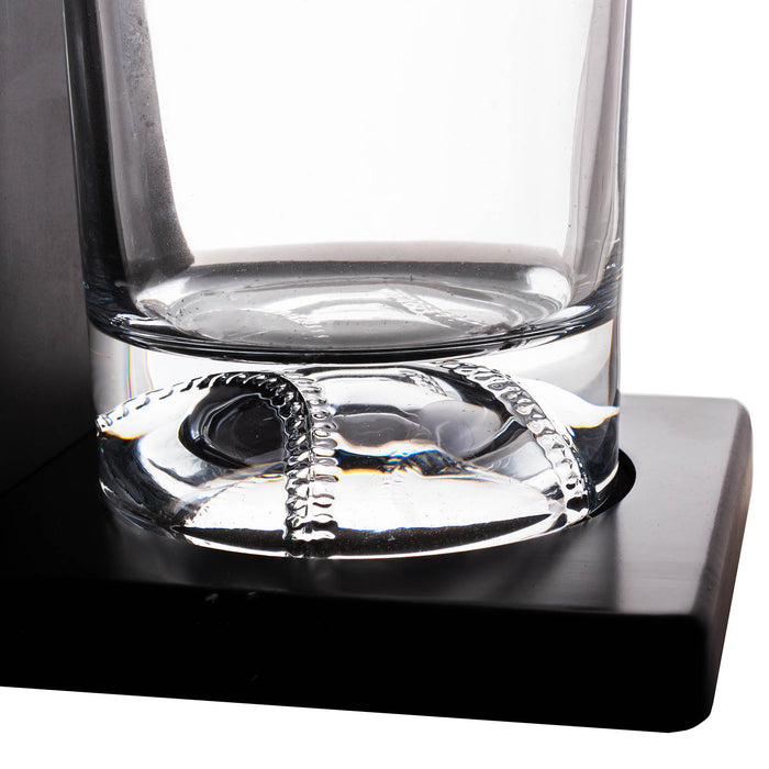Clear glass tumbler with a thick base resting on a black square coaster or stand, photographed against a white background.