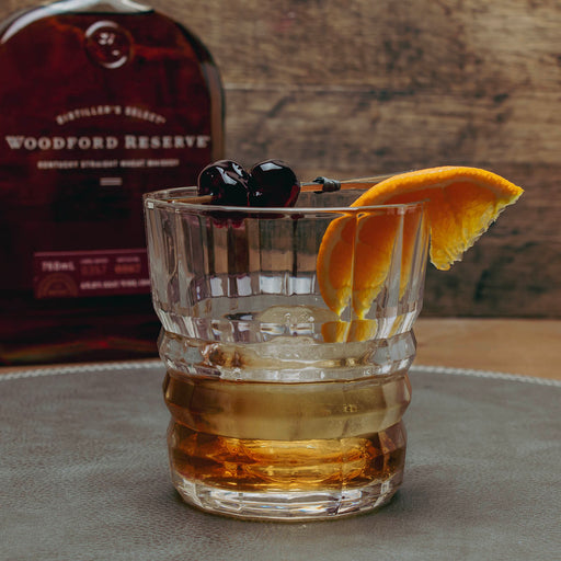 Glass of whiskey with orange slice and cherries in front of Woodford Reserve bottle