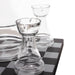 Clear glass chess-piece-shaped candle holders arranged on a black-and-white checkered surface against a white background.