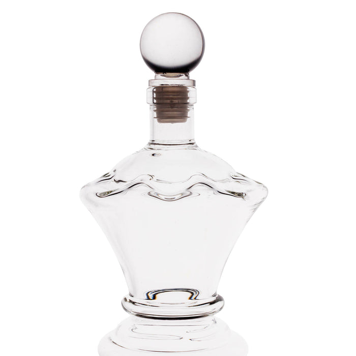 A clear glass decanter with a decorative wavy pattern on the body, a flared base, and a round glass stopper, shown on a white background.