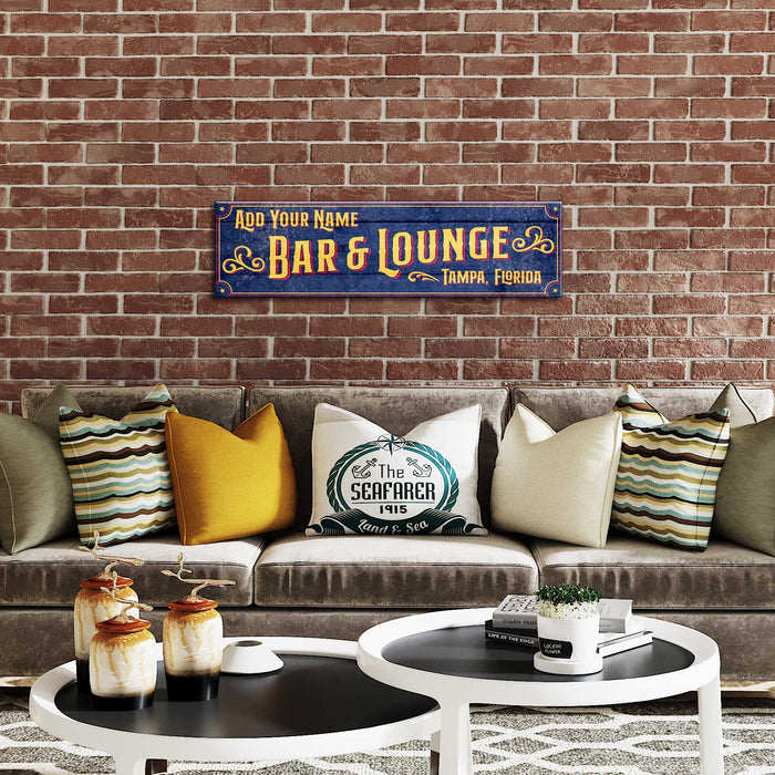 Decorative sign for a bar and lounge above a couch with pillows against a brick wall.