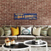 Decorative sign for a bar and lounge above a couch with pillows against a brick wall.