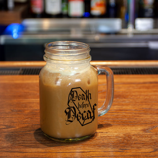 Glass mug with coffee and 'Death Before Decaf' text on a wooden bar.