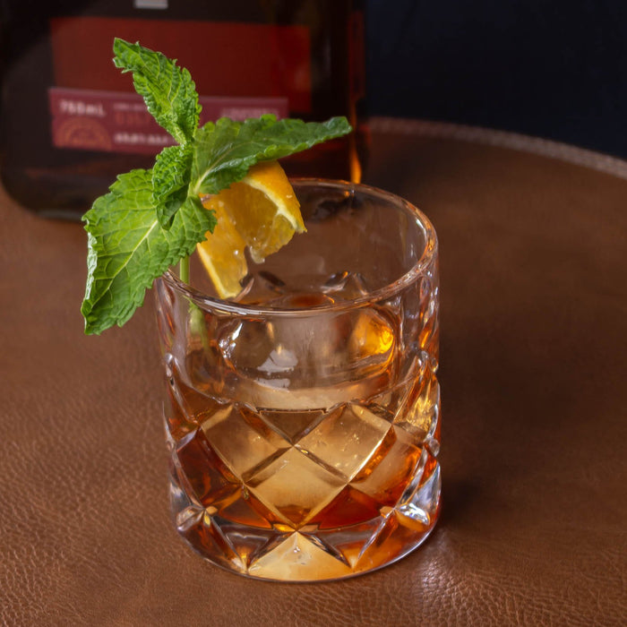 Glass of amber liquid with lemon and mint on a brown surface