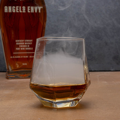Glass of whiskey with ice cubes next to a bottle of Angels Envy bourbon.