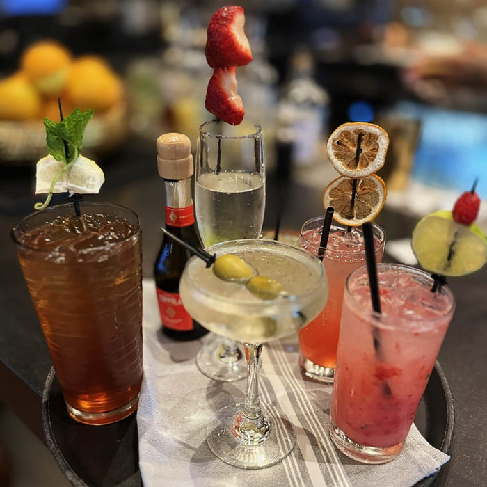 Assorted cocktails on a bar with garnishes and bottles in the background