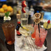 Assorted cocktails on a bar with garnishes and bottles in the background