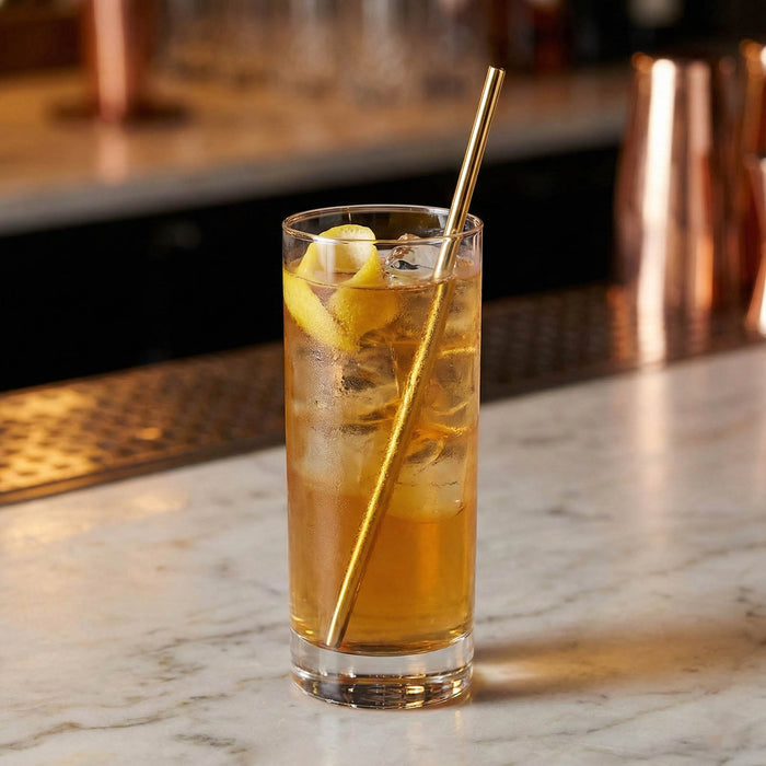 Glass of iced tea with lemon slices and a gold straw on a marble surface.