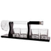 A clear glass decanter with a black handle and four matching clear glass tumblers on a black base, with a clear slotted scoop or spoon resting on the left side, photographed on a white background.