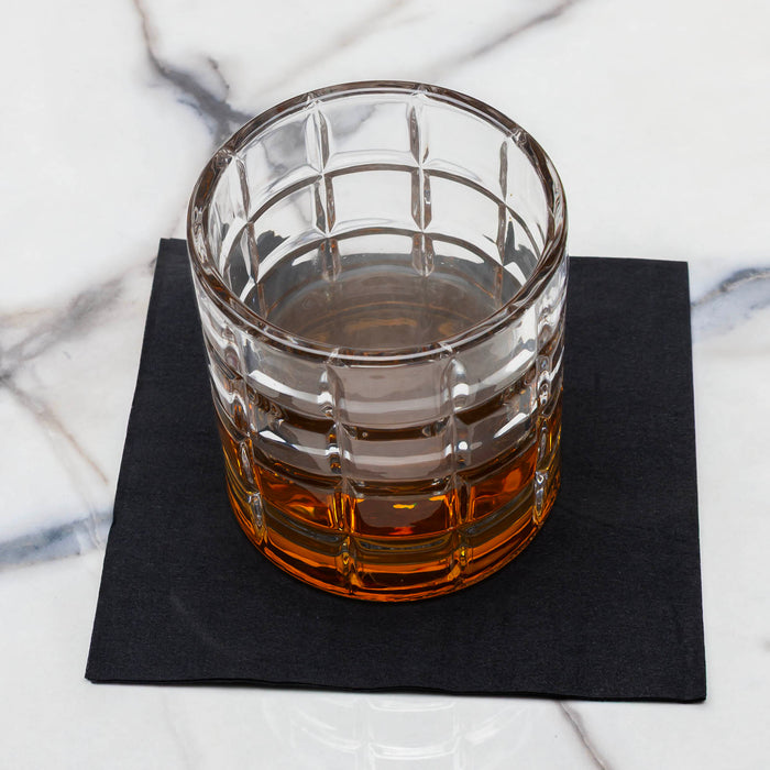 Glass with amber liquid on a black coaster against a marble background