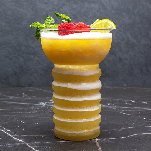 Yellow cocktail in a ribbed glass with garnishes on a dark surface