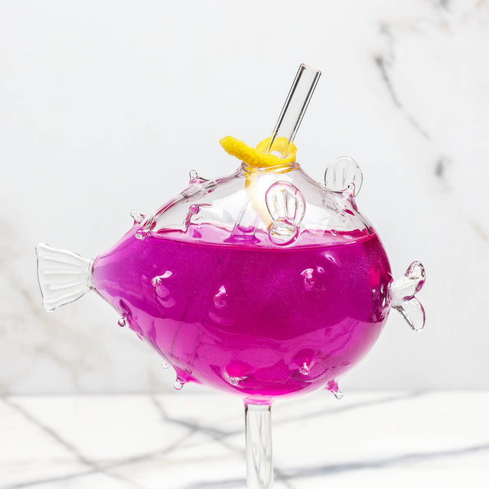 Pink cocktail in a fish-shaped glass with lemon twist on a marble background