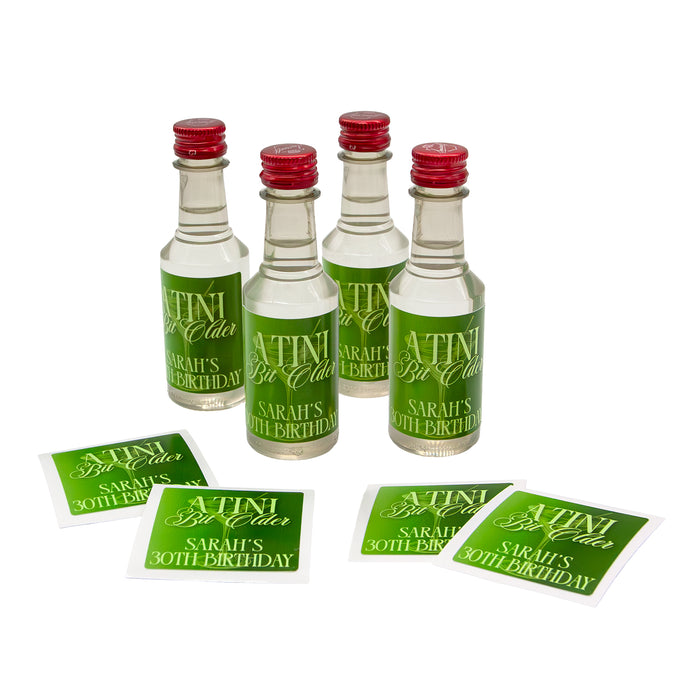 Four mini bottles with red caps and personalized labels 'A Tini Bit Older' on a white background.
