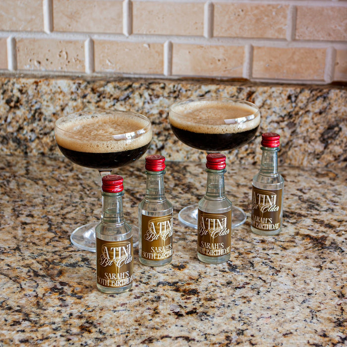 Four mini bottles of 'Tini' with 'Sarah's Birthday' label on a granite countertop.