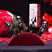 Set of four silver wine bottle stoppers on a red stand with a bottle and roses in the background.